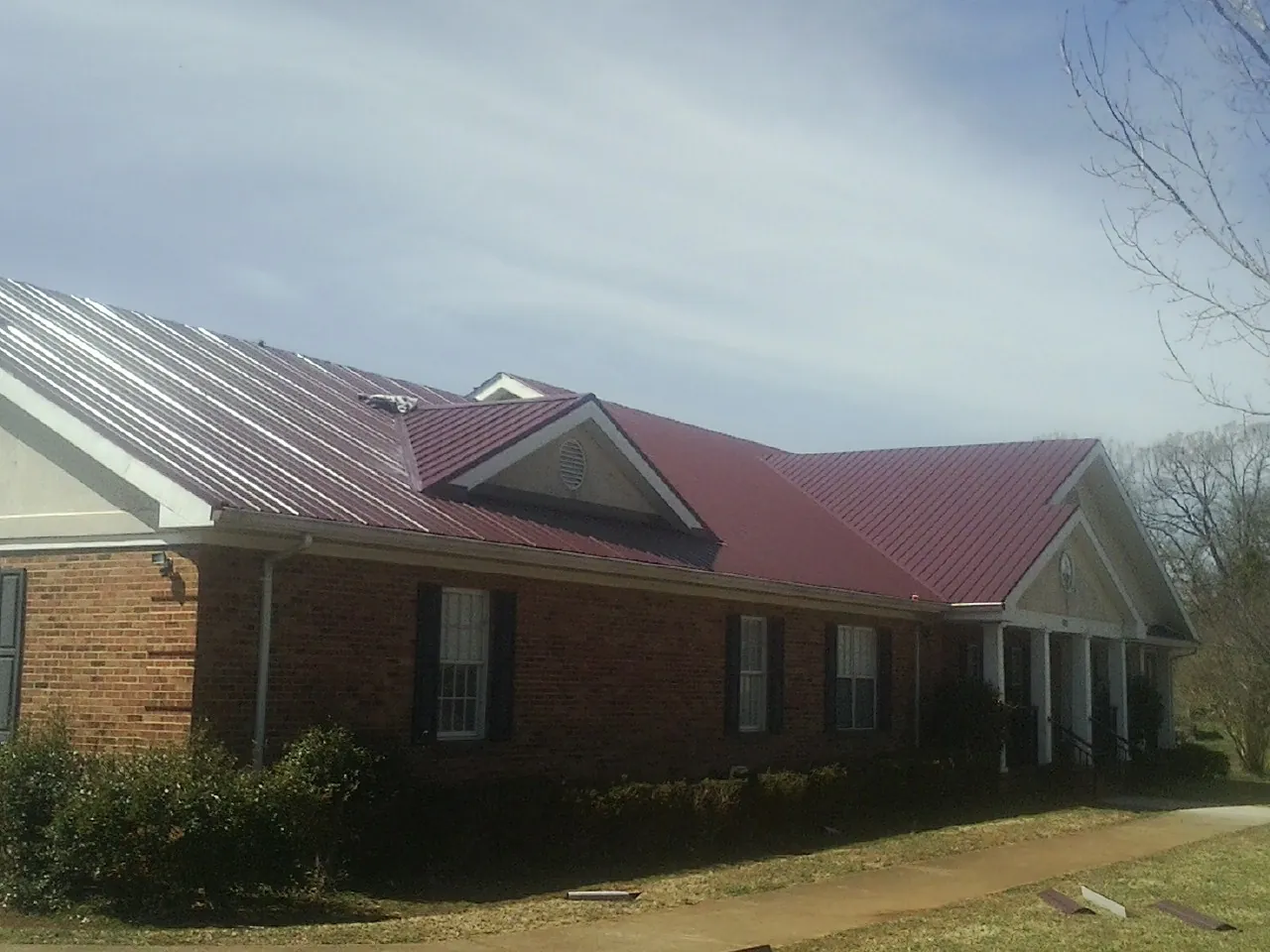 Red metal roof with gabled entries on a long brick building, from a Hail Damage Roof Repair job in Guilford