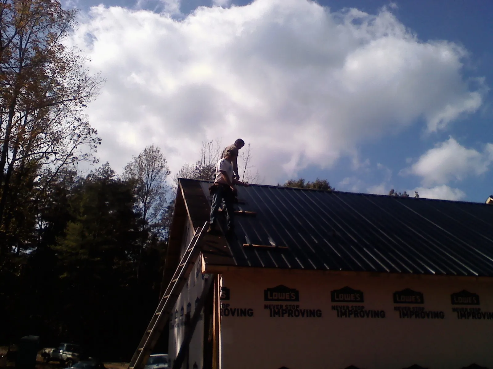 Roofer fastening dark metal panels high against a cloudy sky, from a Roof Inspection job in Guilford