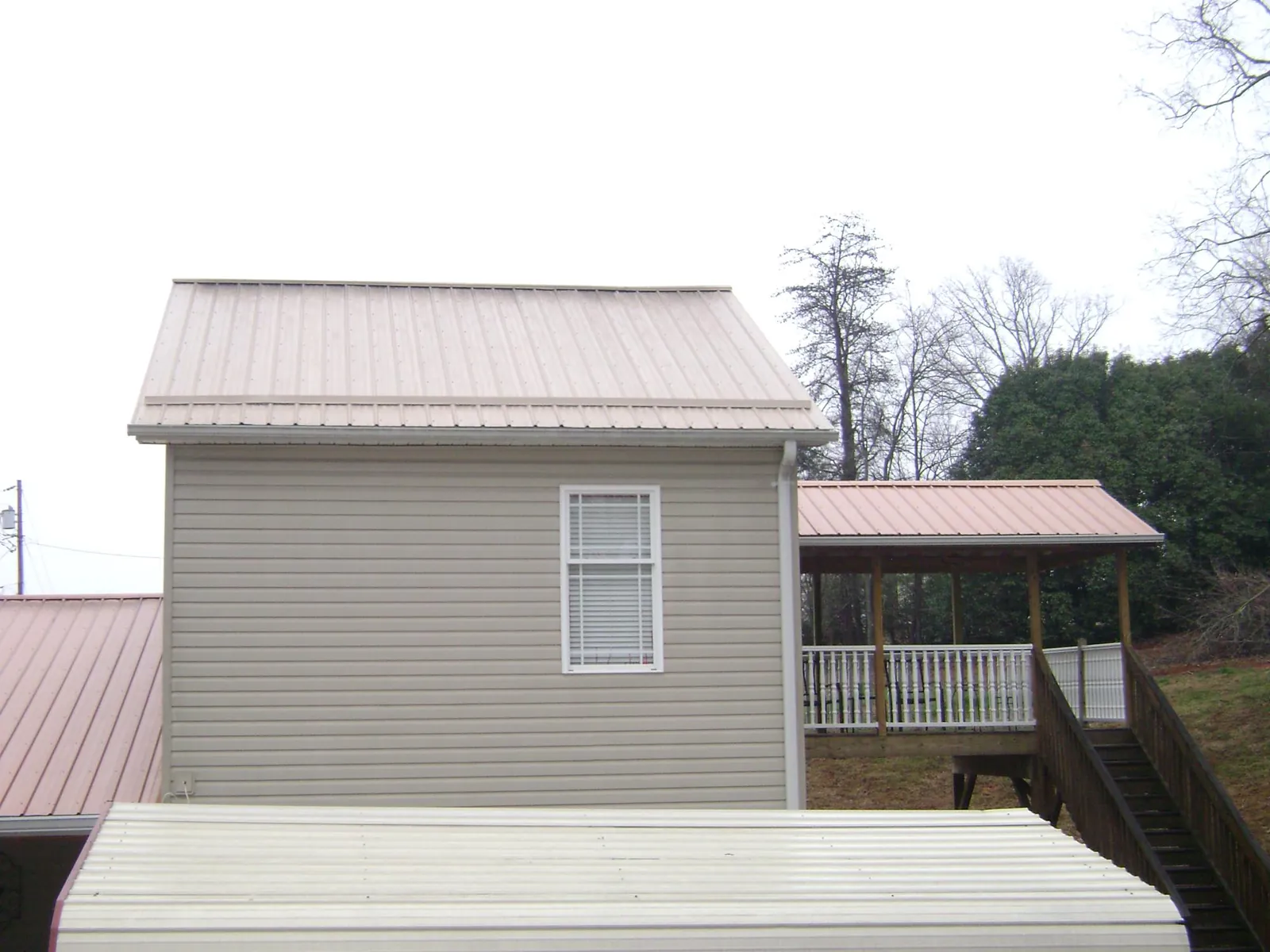 Tan metal roofs on a two story addition and attached porch, from a Roof Replacement job in Guilford